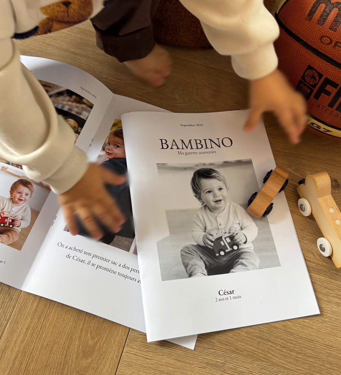 La couverture d'un numéro de Bambino : César, 2 ans et 1 mois, posée sur le parquet entre deux petites voitures en bois